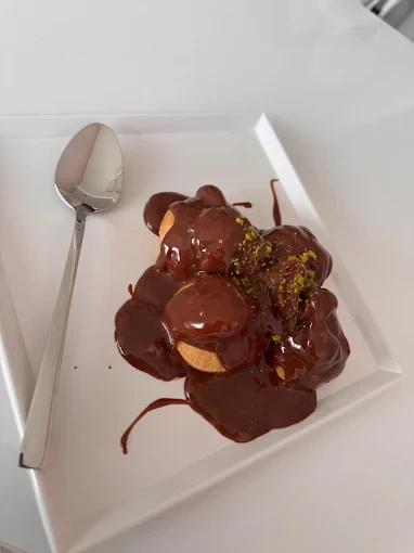 Maye Patissier’in beyaz tabakta çikolata sosu ve fıstık süslemesiyle profiterol sunumu